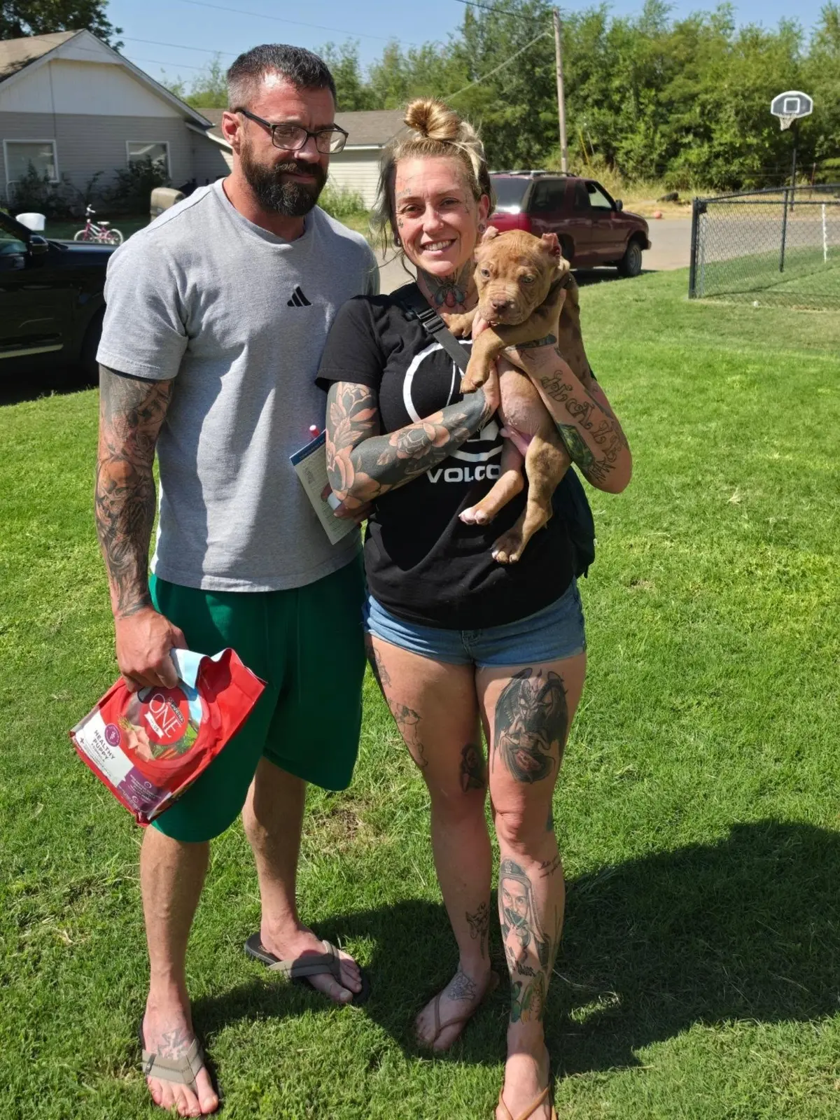 A couple holding their chocolate puppy on the lawn